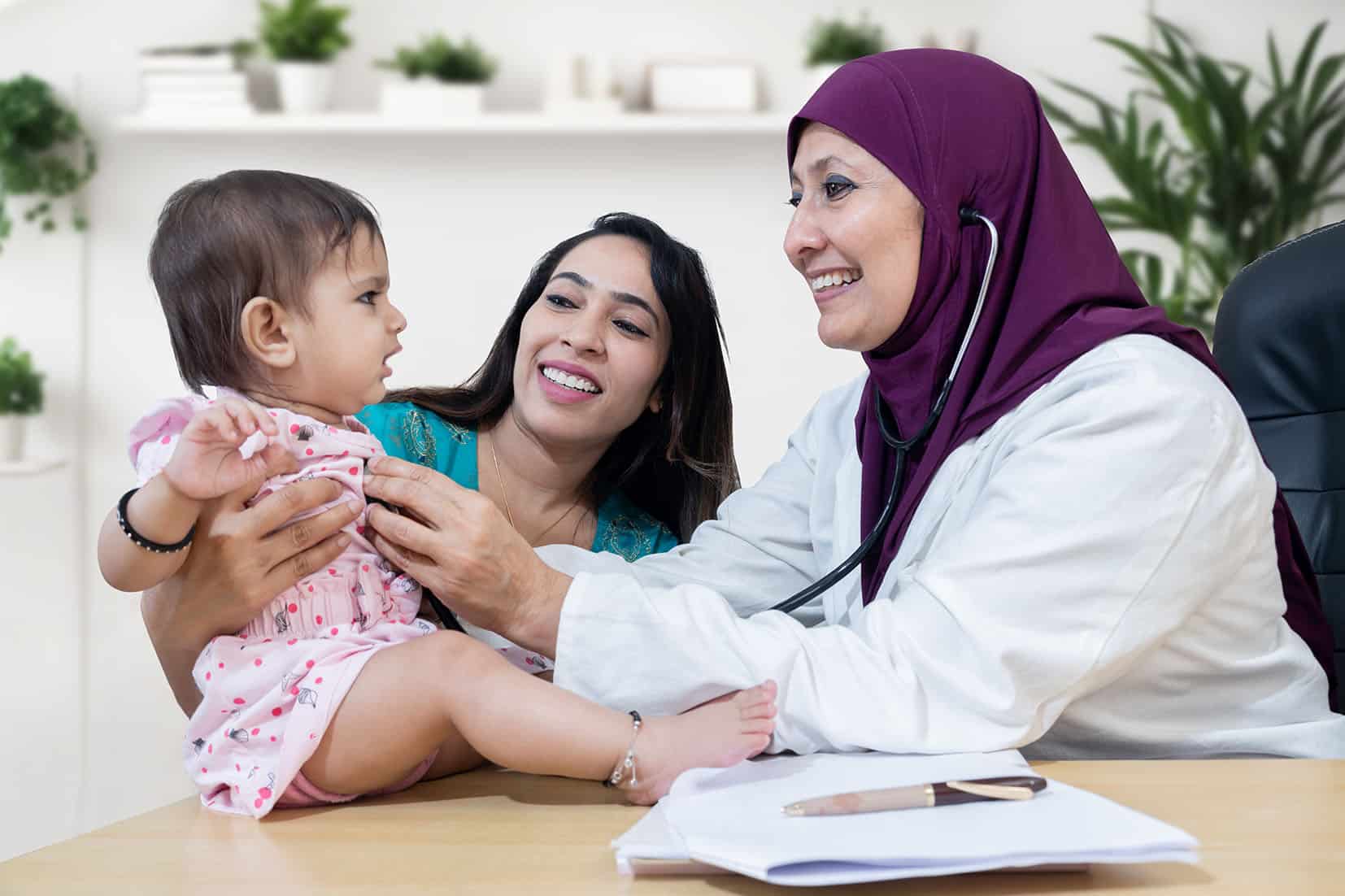 young indian mother with her cute little baby visiting female muslim general pediatrician wearing hijab in modern clinic for routine check up, healthcare and medical concept.
