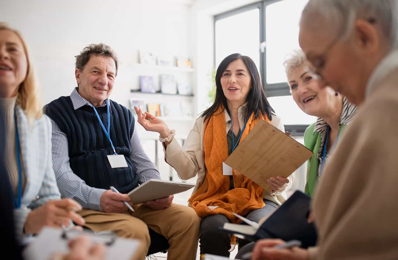 excited elderly people attending group therapy session at nursing house, positive senior man and woman sitting in circle, having conversation with psychologist