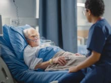 hospital ward: friendly head nurse connects finger heart rate monitor or pulse oximeter to elderly patient wearing oxygen mask resting in bed. nurse does patient checkup after successful surgery