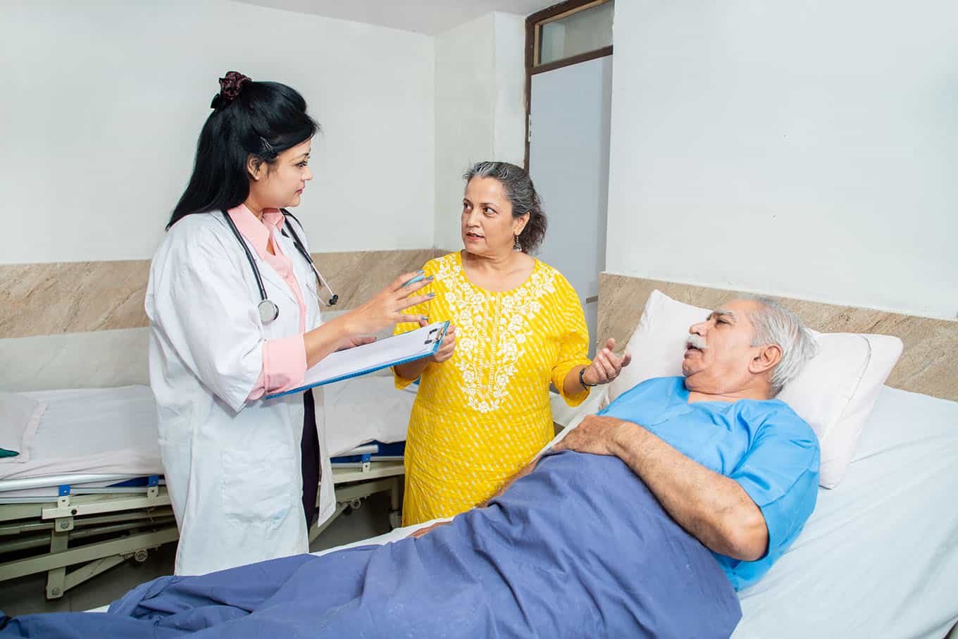 indian doctor talk to olde senior male patient's wife at clinic or hospital regarding the improvement of health condition of her husband, elderly people health care concept.